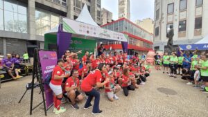 Pessoas em frente a um palco pousando para foto com camisetas vermelhas após participarem da 5ª edição da Corrida Pela Doação de Órgãos em São paulo.